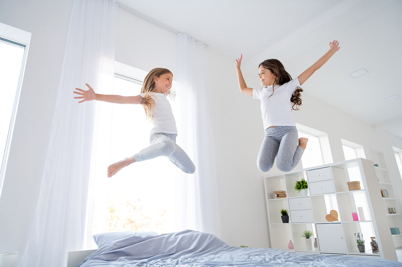 Šťastné deti skáču na nízkej posteli v spálni s vysokými stropmi