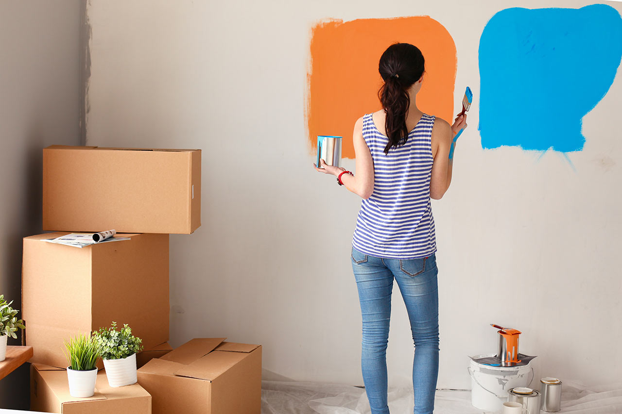 Mladá žena maľuje interiér v kombinácii oranžovej a modrej